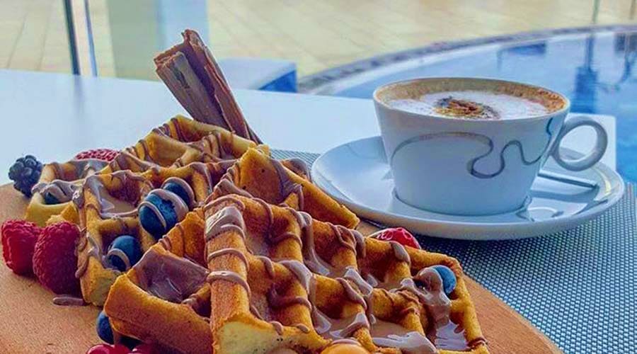 Belgian waffle topped with berries and chocolate sauce served with cappuccino at a luxury beachfront venue